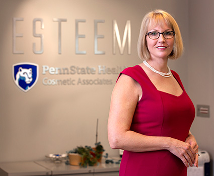 Dr. Jessyka Lighthall is standing in front of a desk. Pictured behind her is Esteem Penn State Health Cosmetic Associates signage on the wall.