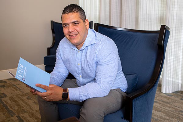 A man is seated in a chair in the "Esteem" lobby while reading an "Esteem" brochure.