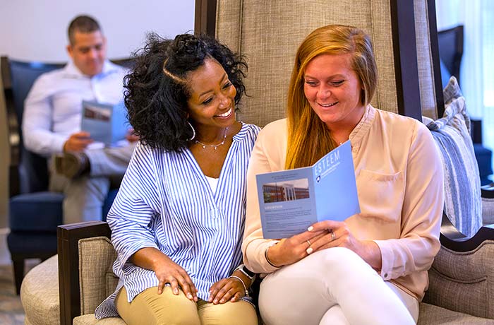 Two patients are reading an “Esteem” brochure while seated in the "Esteem" waiting room. Another patient is pictured seated in the background.